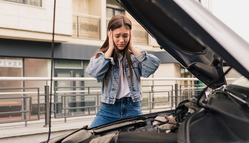 девушка заглядывает под капот и держится за голову