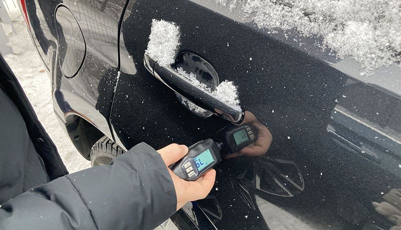 мужчина измеряет толщиномером дверь автомобиля