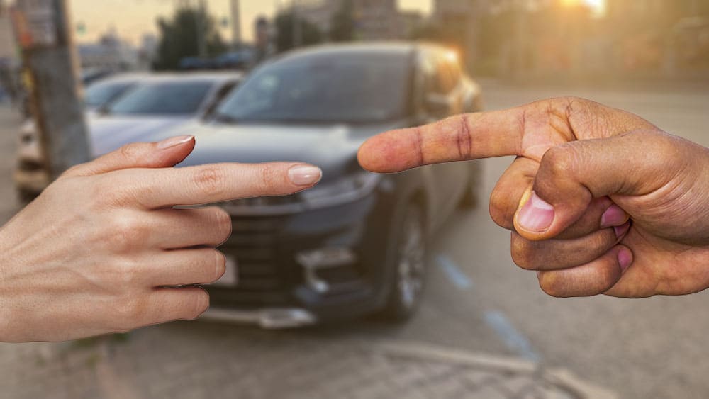 мужчина иженщина показывают друг на друга пальцами, на заднем плане автомобиль