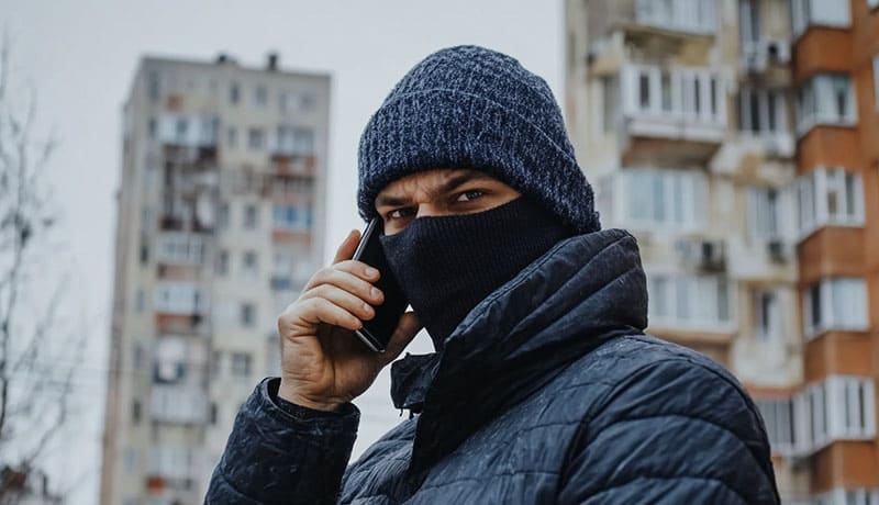 мошенник разговаривает по телефону рядом с многоэтажками
