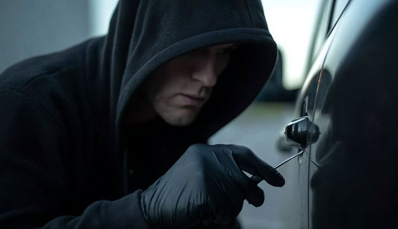 мужчина в черном капюшоне взламывает машину