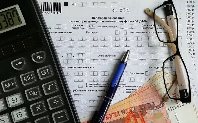 налоговая декларация, калькулятор, ручка, деньги и очки лежат на столе